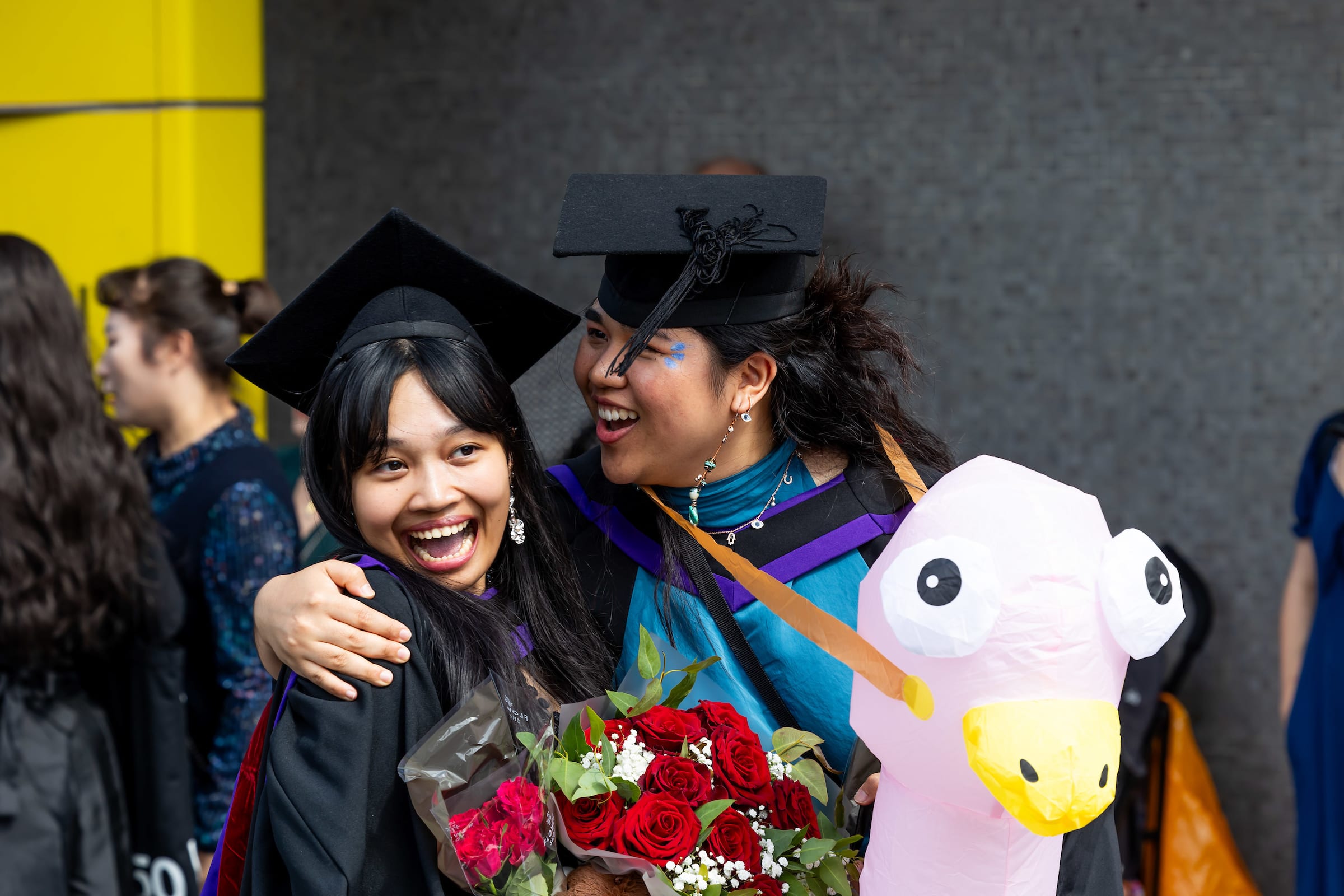 Two grads hug, one is wearing an inflatable ostrich