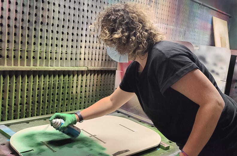 Student spray-painting a piece of wooden prototype.