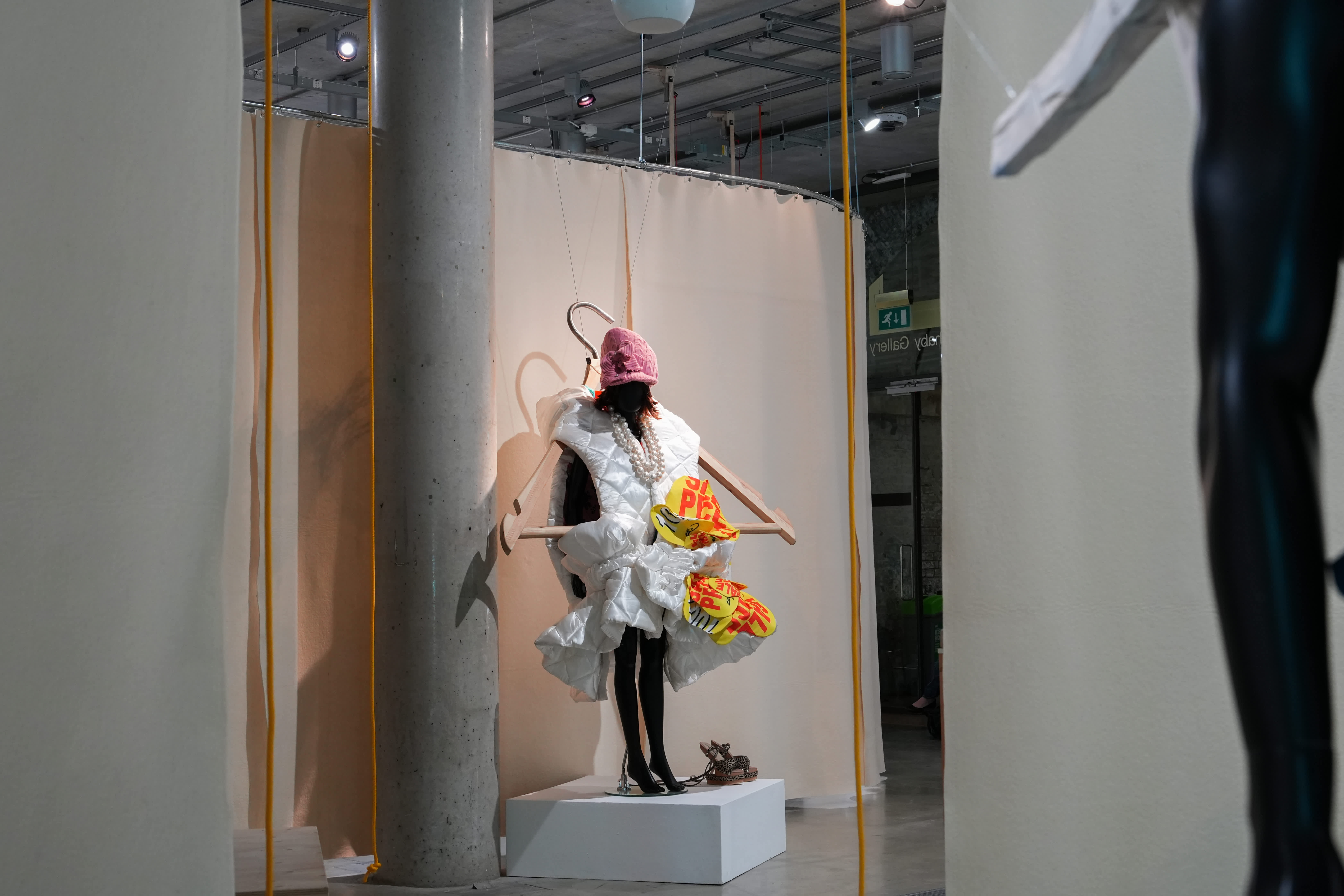 A mannequin displaying garments including puffy white outerwear, a wooly pink hat, a staff and colour flowers
