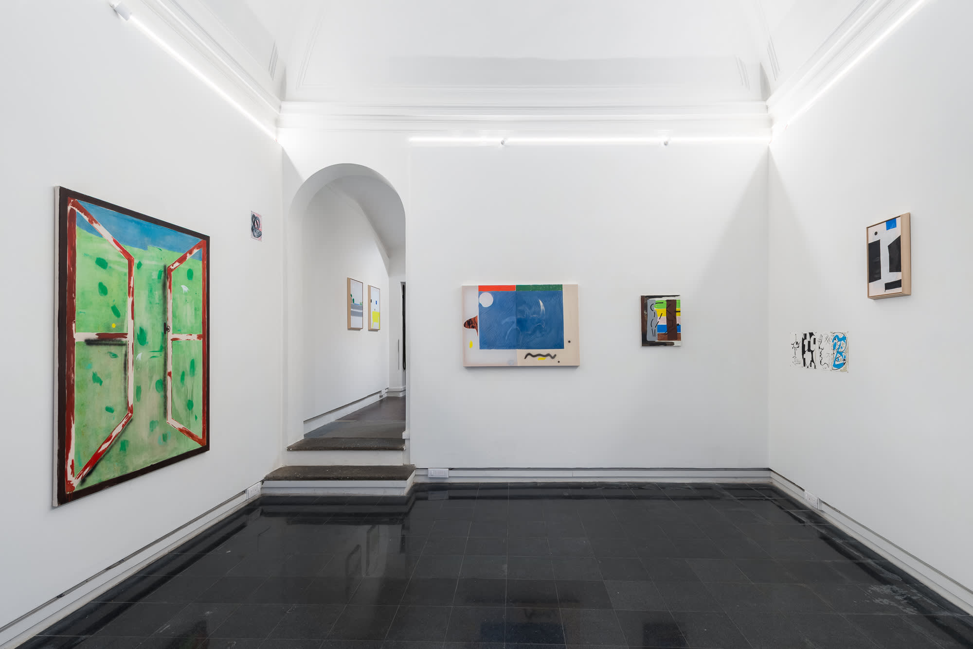 Installation view of a gallery exhibition featuring colourful abstract paintings and mixed-media artworks displayed on white walls, with an arched doorway leading to an adjacent gallery space.