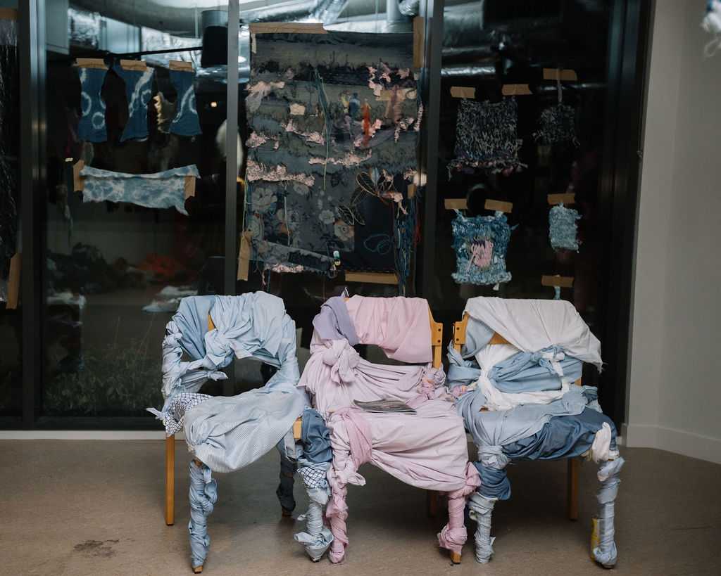 Image of an art installation using clothes woven around chairs