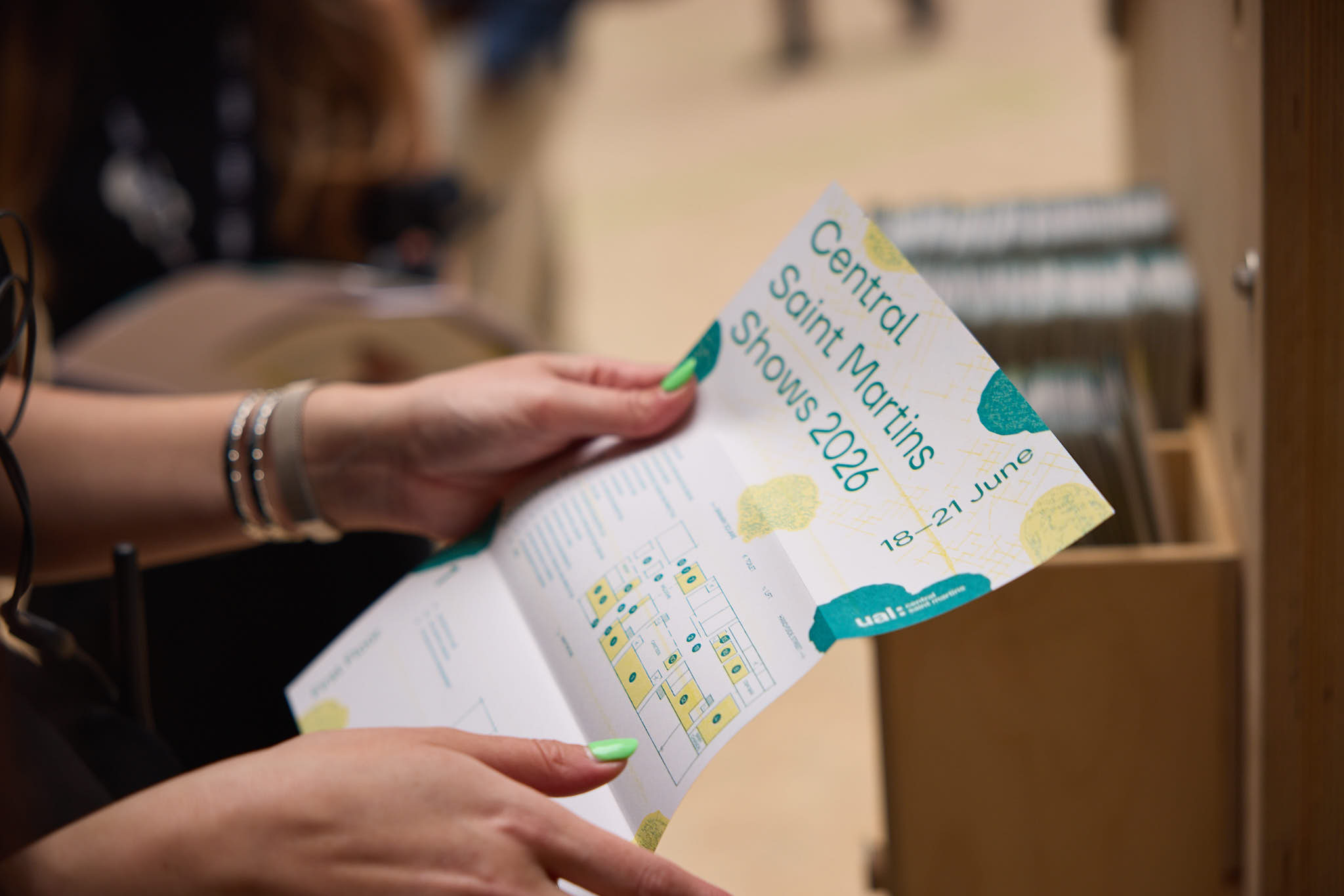 Close-up of hands holding a folded event leaflet titled “Central Saint Martins Shows 2026,” with dates “18–21 June,” showing a map and venue details inside.