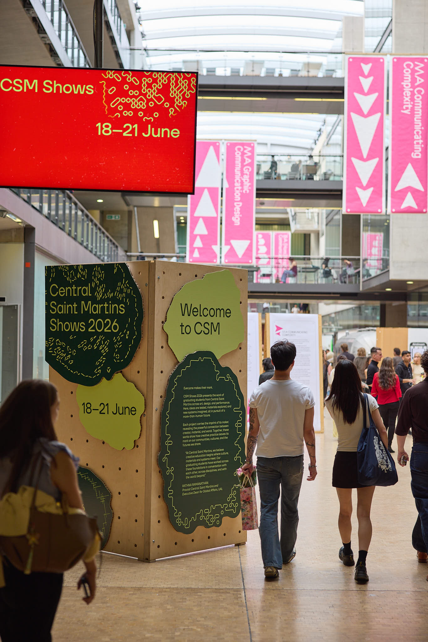 Interior of a busy exhibition space at Central Saint Martins with visitors walking past a large sign reading “Central Saint Martins Shows 2026, 18–21 June” and banners hanging above.
