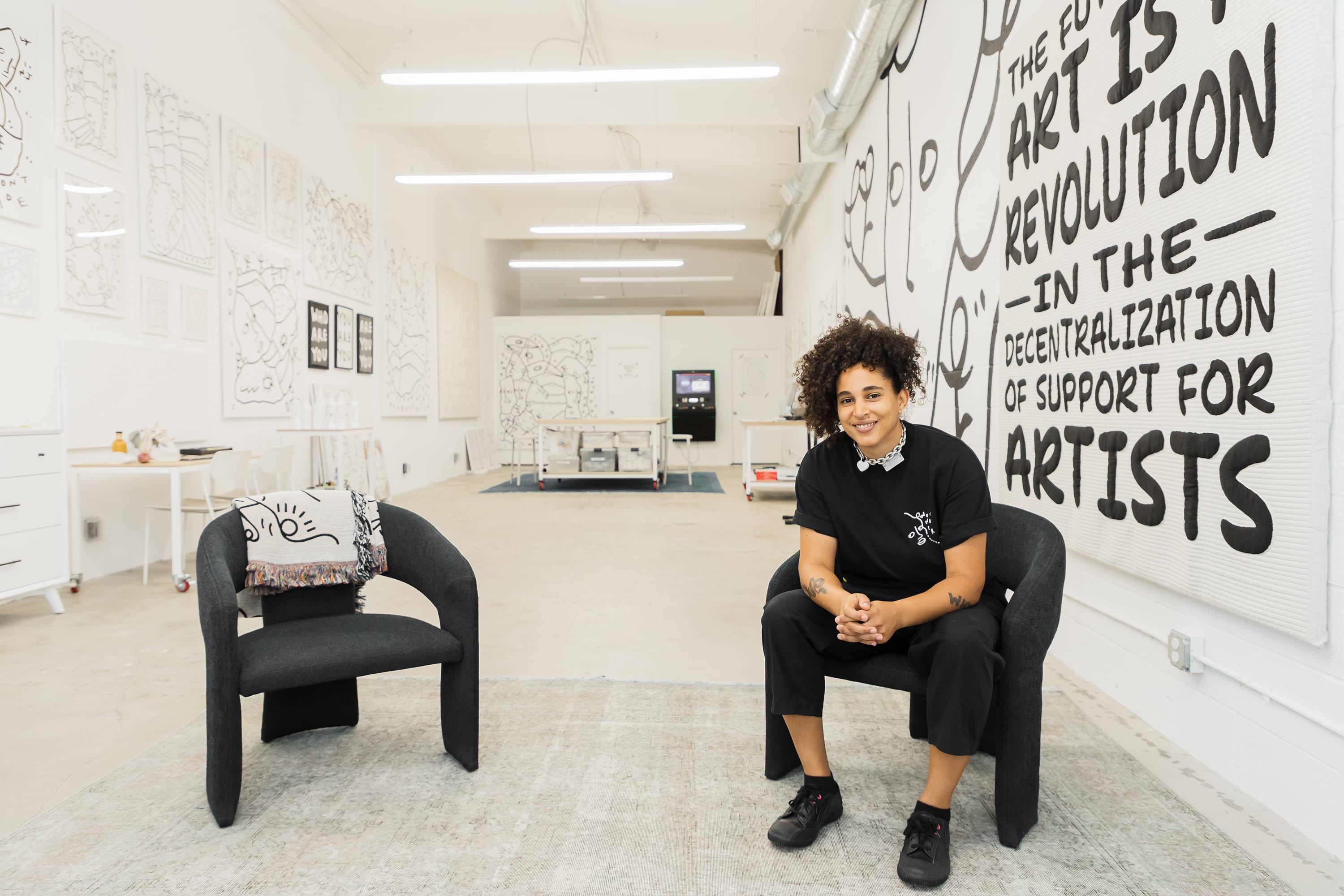 A woman sits on a armchair infront of black and white pieces of art