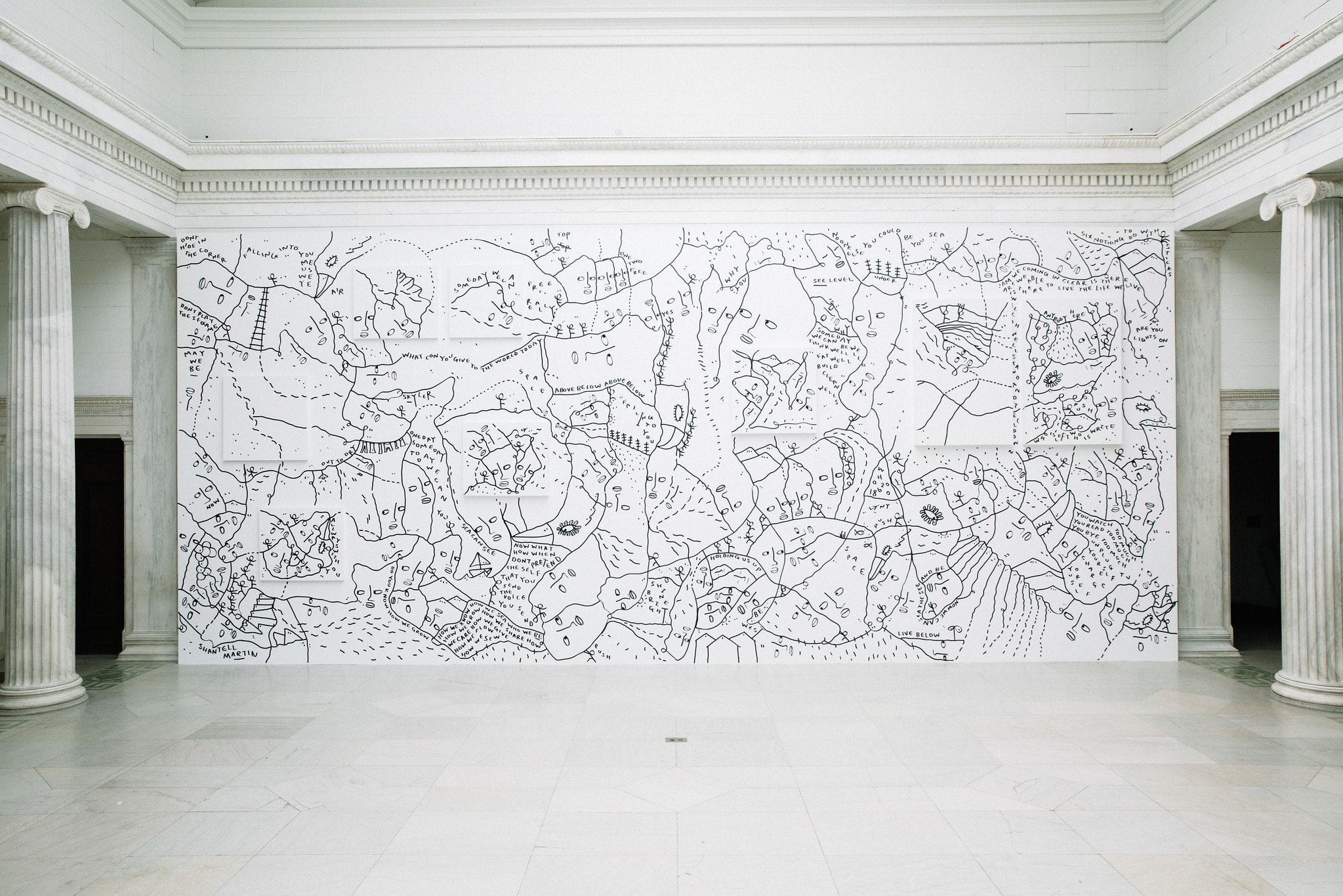 A white wall of filled with drawings. The drawings are in black against a white wall