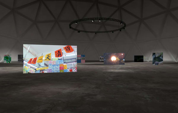 Screen shot of a virtual exhibition room which appears to be a large dome with a circle of lighting hanging from the ceiling. In the foreground is a large free-standing photograph of some bunting with Chinese characters on. Other works are visible in the background.