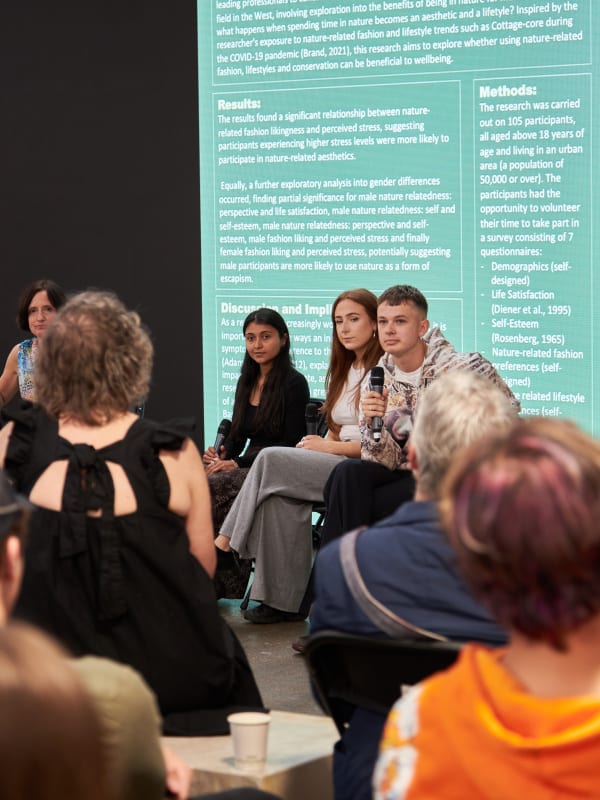 Panel of four speaking to a crowd with screen behind them