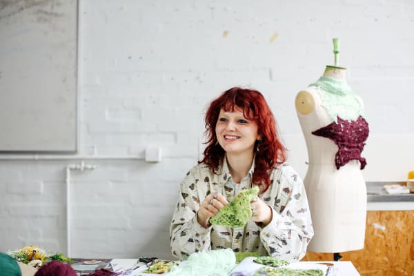 Sydney wearing a shirt covered in a pattern of bugs while knitting and chatting.