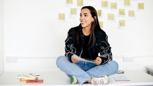 Lady sat cross legged on white tabletop looking to the left in classroom setting