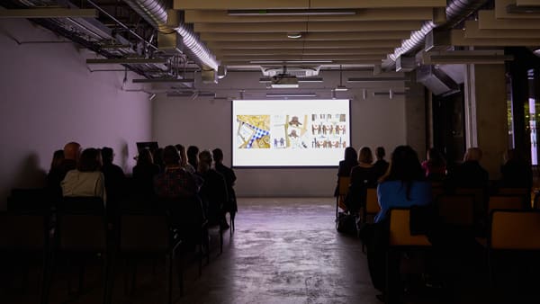 Long audience shot of people on the left and right and a big projector screen in the middle.