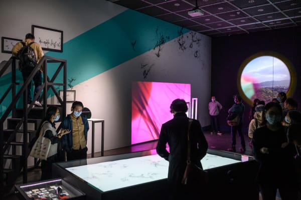 People stood looking at an instillation with various screens and colours 