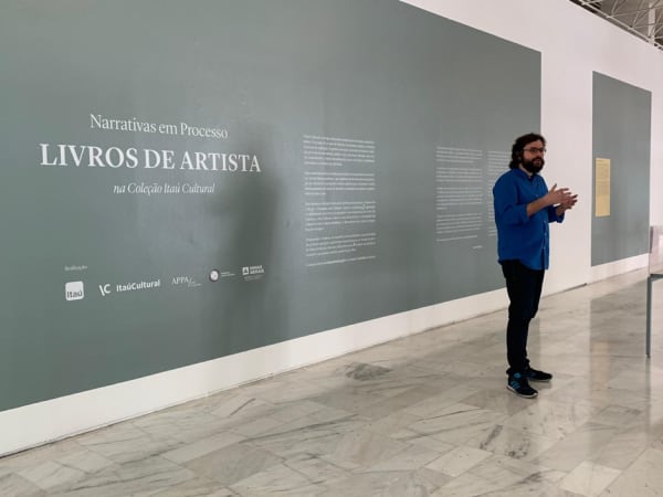 A casually dressed professor shot against a large internal grey wall with Portuguese writing 