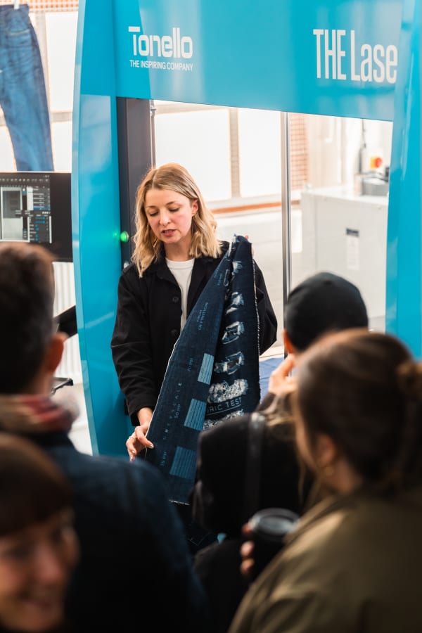 a person holding a piece of denim fabric with a pattern on it infant of a big machine and people