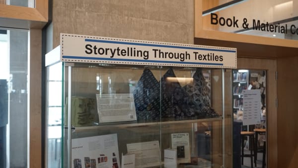 Glass shelf in a library with textile objects inside.