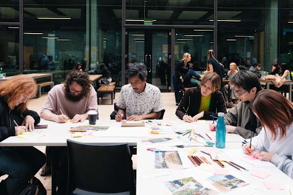 An image of people sitting around a desk and writing 