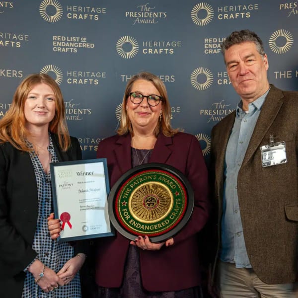 3 people smiling at camera, person in the middle holding certificate and plaque.