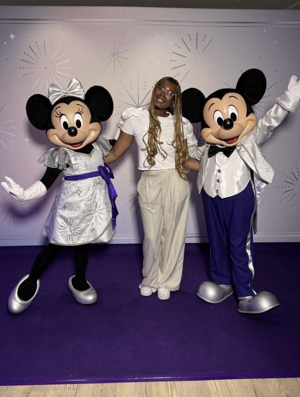 Preye standing on a stage between Mickey Mouse and Minnie Mouse life-size characters. 