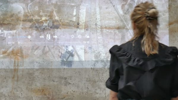 person with a blonde ponytail looking at a film being projected onto a wall