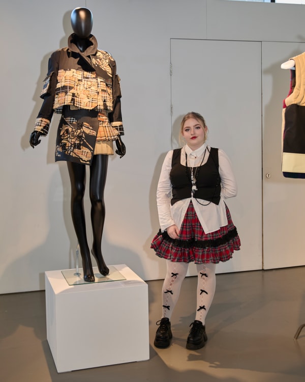 Person smiling at camera, standing next to mannequin with blazer and skirt on.