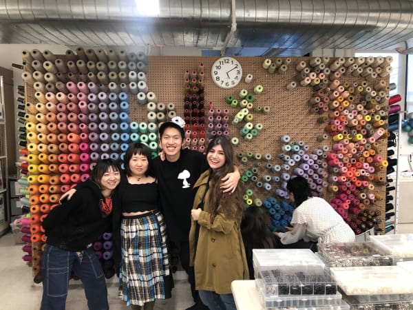 Four people smiling at the camera infront of a wall of colourful threads 