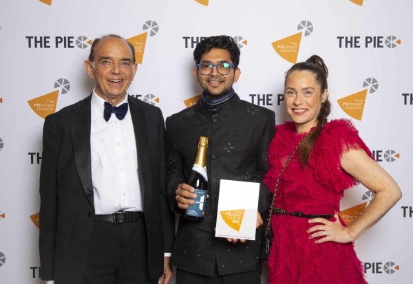 3 people smiling at camera. Central person holding plaque and bottle of champagne.