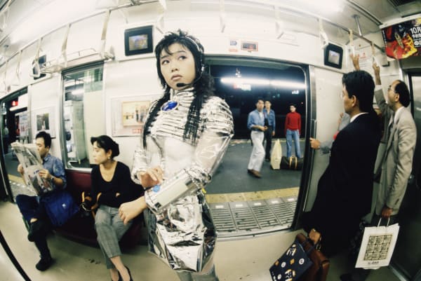 Image shows a woman dressed in a silver spacesuit on board a crowded subway cart.    