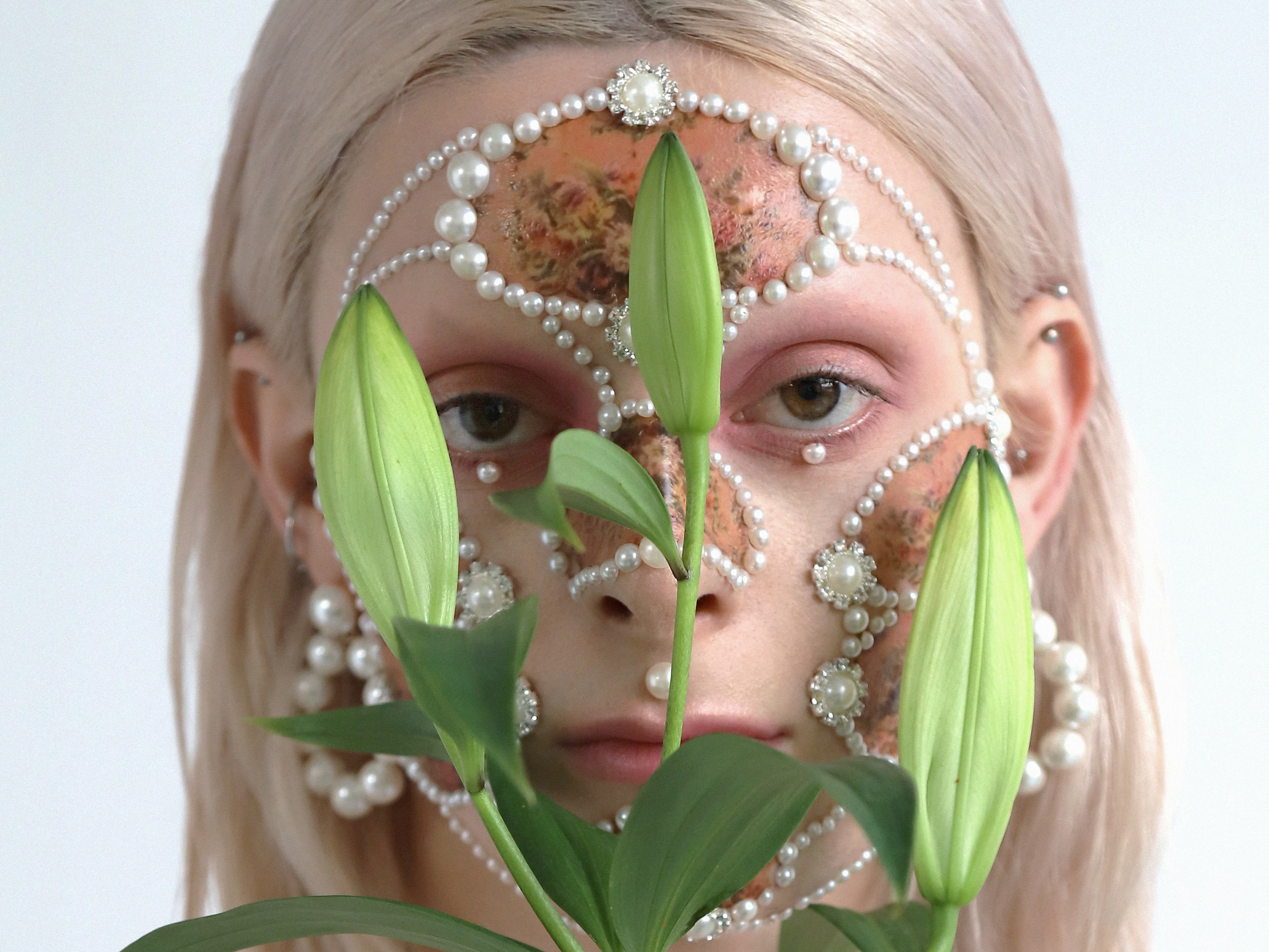 Female model with pearl facial jewellery, makeup and lilies.