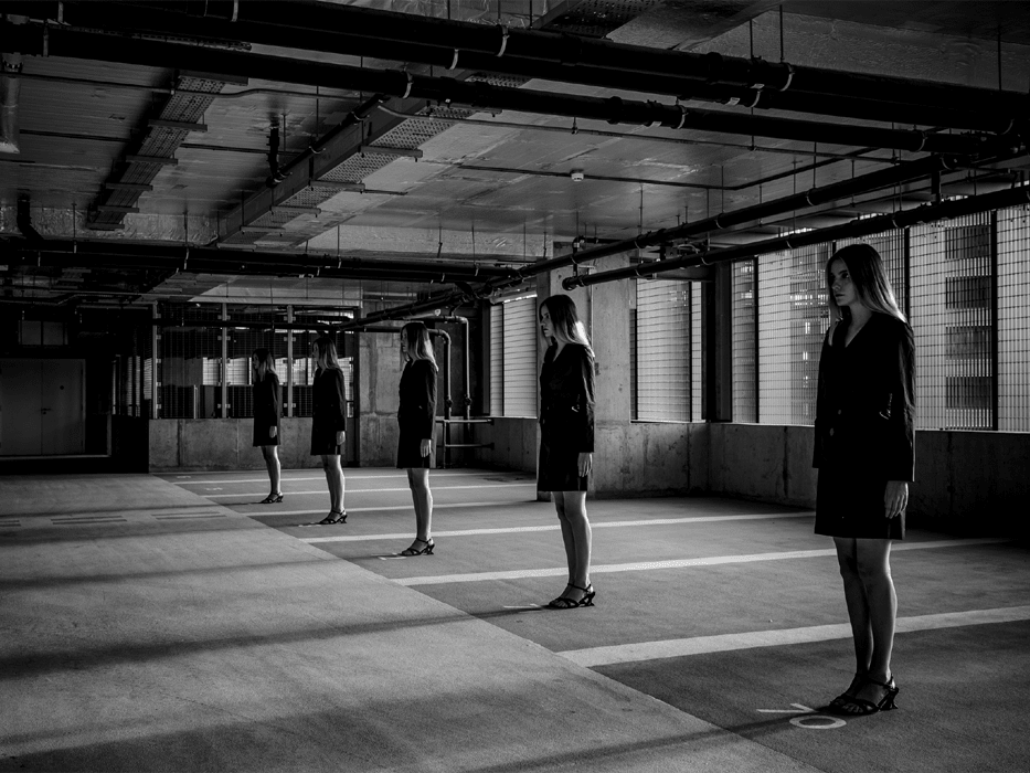 Black and white photograph of models standing in a line in a carpark-style building.