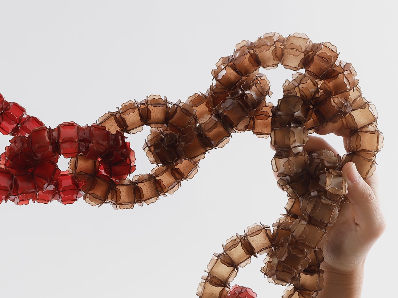 Two hands holding up a red-coloured interlinked piece of jewellery.