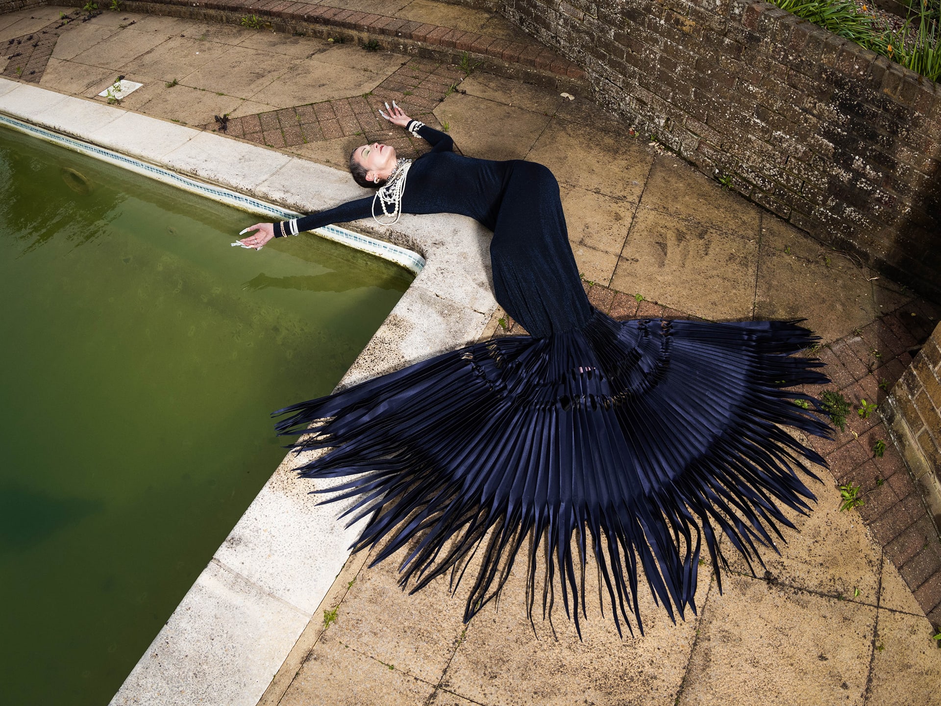 Woman lying across poolside draped in blue spikes dress