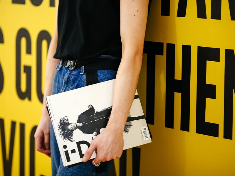 Zoomed into the lower half of a person and a hand holding a fashion book
