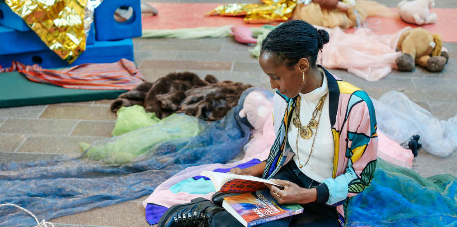 A person sits on the floor surrounded by colourful material