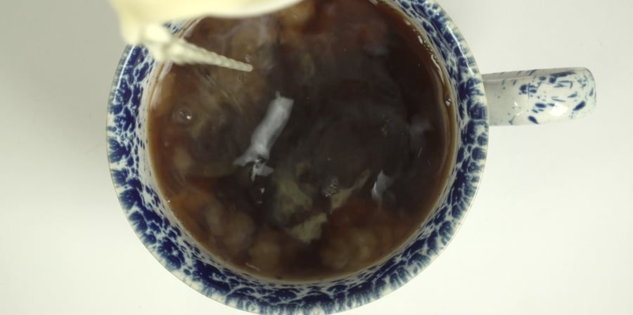 A still of milk being poured into a teacup.
