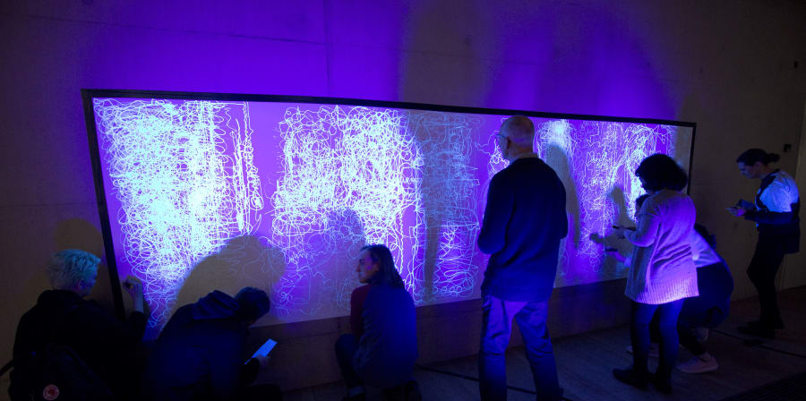 People standing in front of a screen in a purple-lit room 