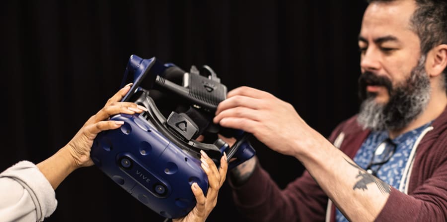 A technician passes a VR headset to a student.