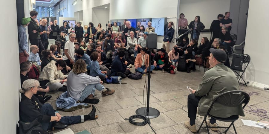 An audience surrounding a sitting presenter in an exhibition hall.