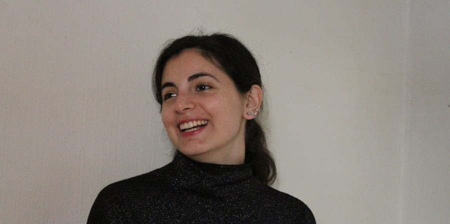 Woman in a black polo-necked jumper, against a white background. 
