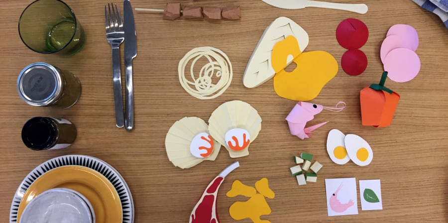 Pieces of food made out of paper lying on a table with cutlery