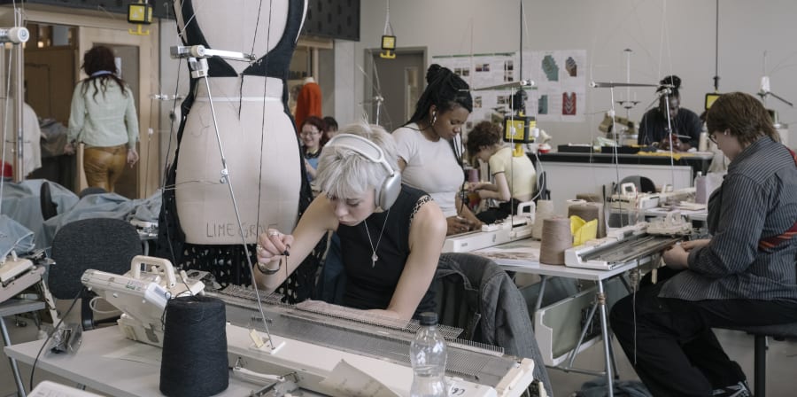 People using sewing machines, with a mannequin in the middle of the room.