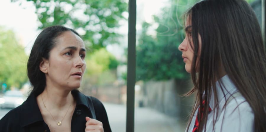 A mother and daughter stare at each other at a bus stop.