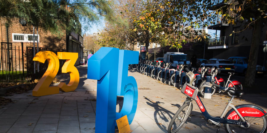 Large colourful numbers standing on a street by a bike hire bay.