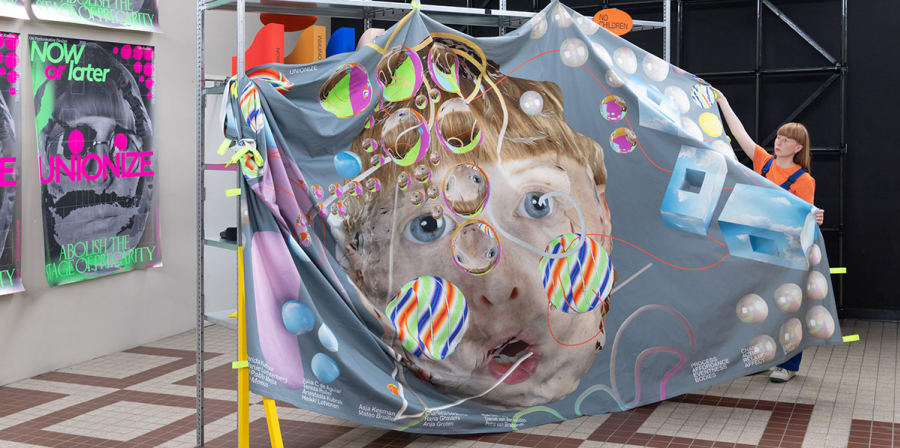 An artist stands beside a bedsheet-sized artwork depicting a face surrounded by coloured bubbles.