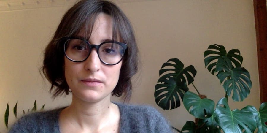 Close up of a woman with short brown hair and glasses , plants in the background