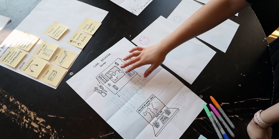 A table is filled with post-it notes, Sharpie pens and plans for a project titled: 'Code Breaker'