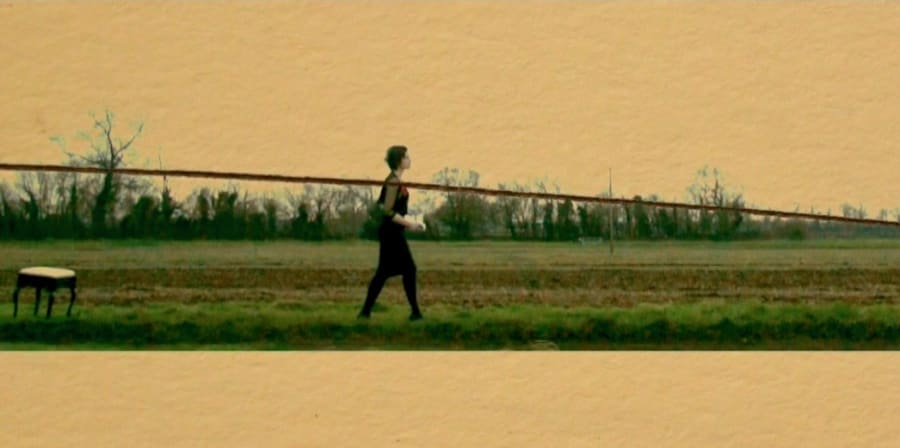 Still image of a woman walking across the field. The image has a horizontal line drawn across as though it.