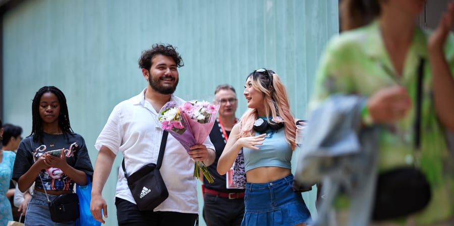 Smiling people entering the College, one is holding a bunch of flowers