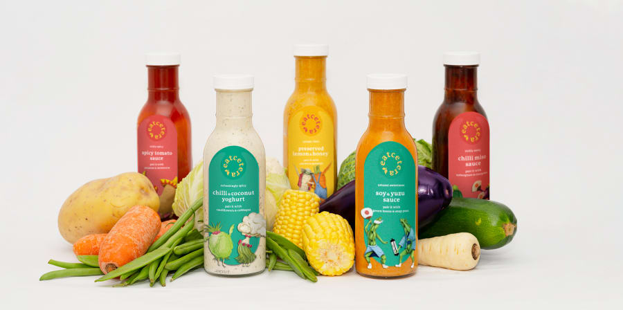 An array of food products including bottles, sitting amongst vegetables.