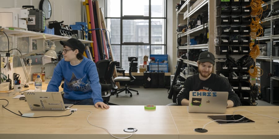 Two people at a desk with laptops, surrounded by equipment such as cameras and screens.
