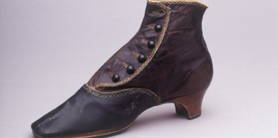 A dark brown ankle boot from the 1870s, with a short heel, five button fastenings and decorative top-stitching.