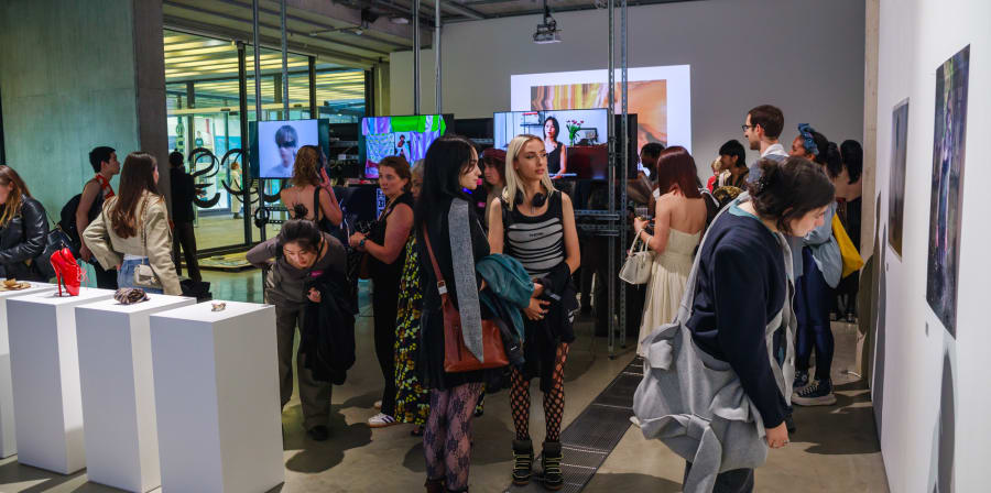 A crowd inside the Lethaby Gallery space with displays on screens and objects on pedestals visible